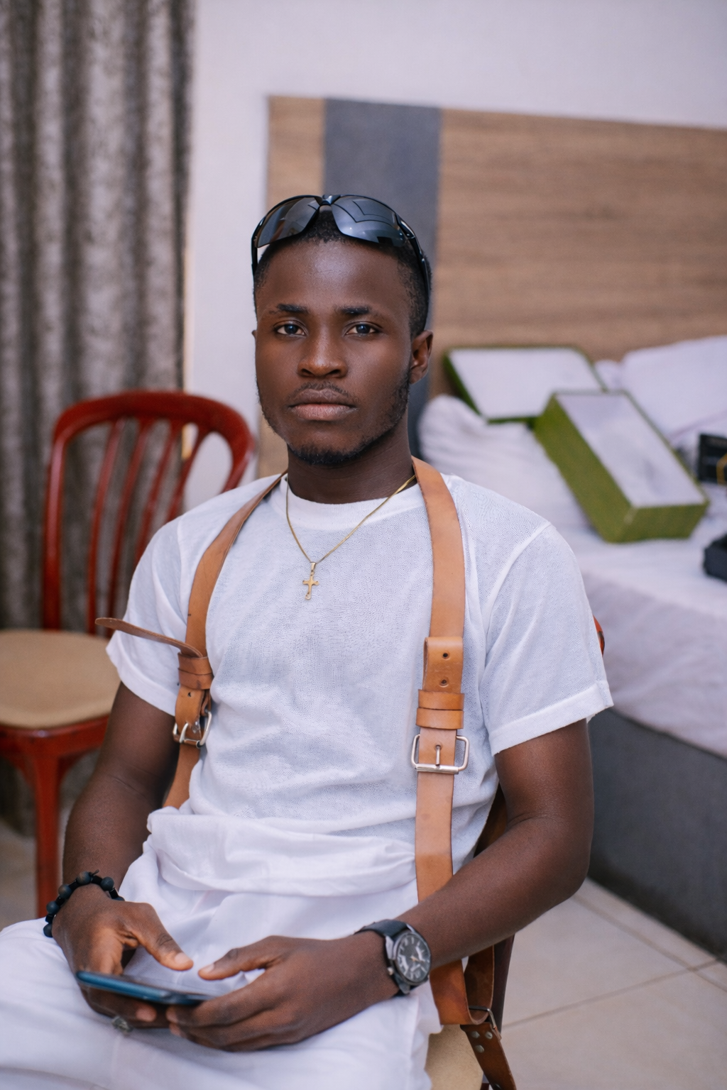 Joshua Adetomiwa, the photographer behind Sir AKJ Photography, seated in a white shirt and tan suspenders.